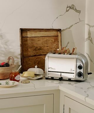 A silver toaster on top of a marble countertop with white cabinets below it