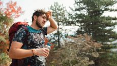 A man wiping sweat from his head whilst out on a hike