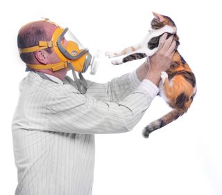 A man wearing a gas mask holds a cat at an arm&#039;s length