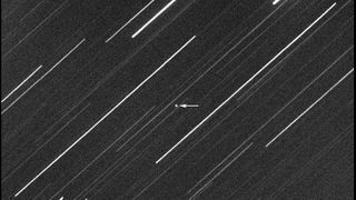 streaks of stars with an asteroid imaged in the middle. an arrow points to the asteroid