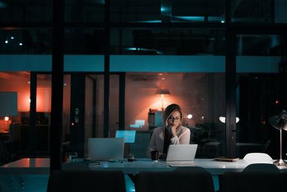 A businesswoman using a laptop at her desk during a late night at work.