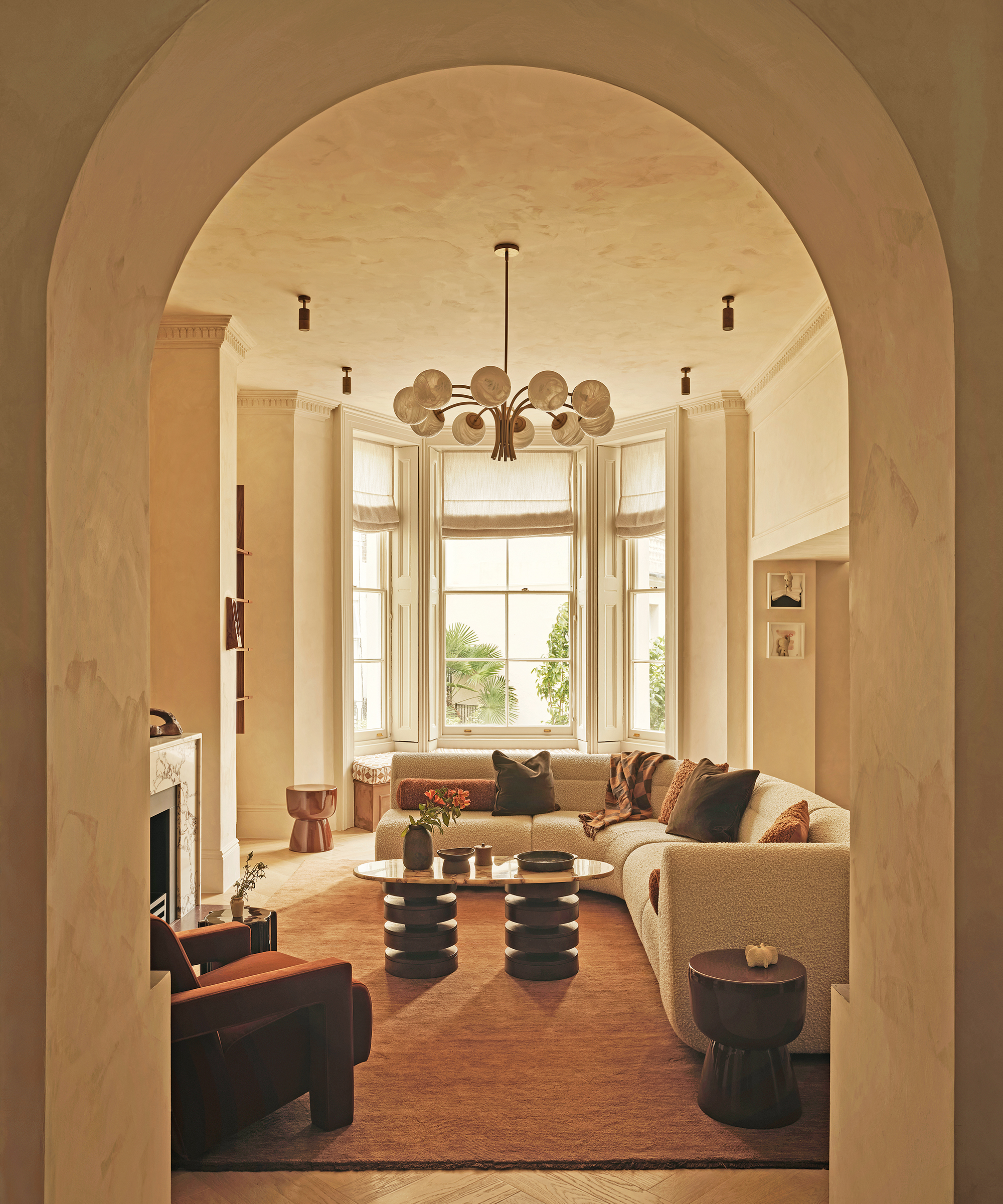 a living room seen through a arched doorway with a large curved white sofa and red rug