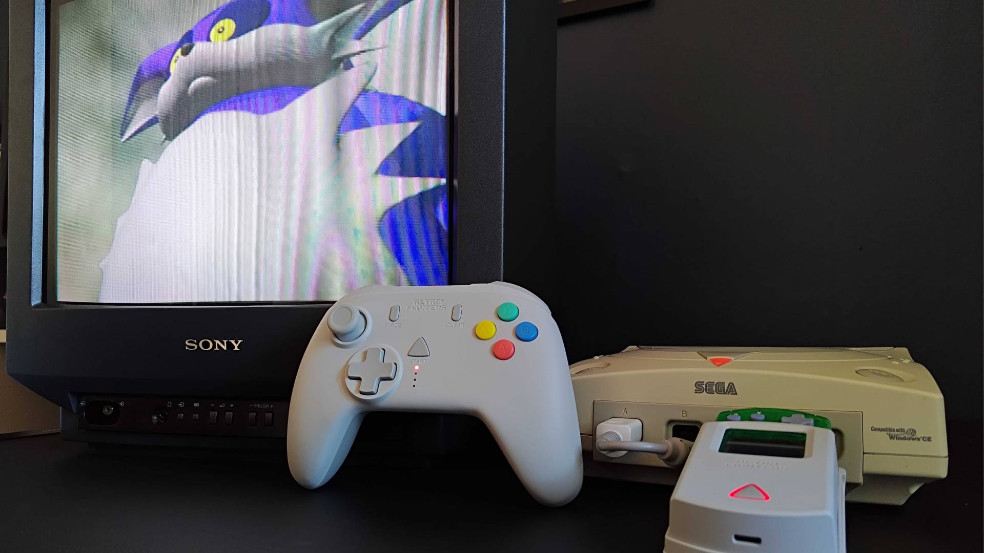 Retro Fighters StrikerDC leaning against Sony Trinitron CRT TV and Sega Dreamcast with Big the Cat from Sonic Adventure on screen.