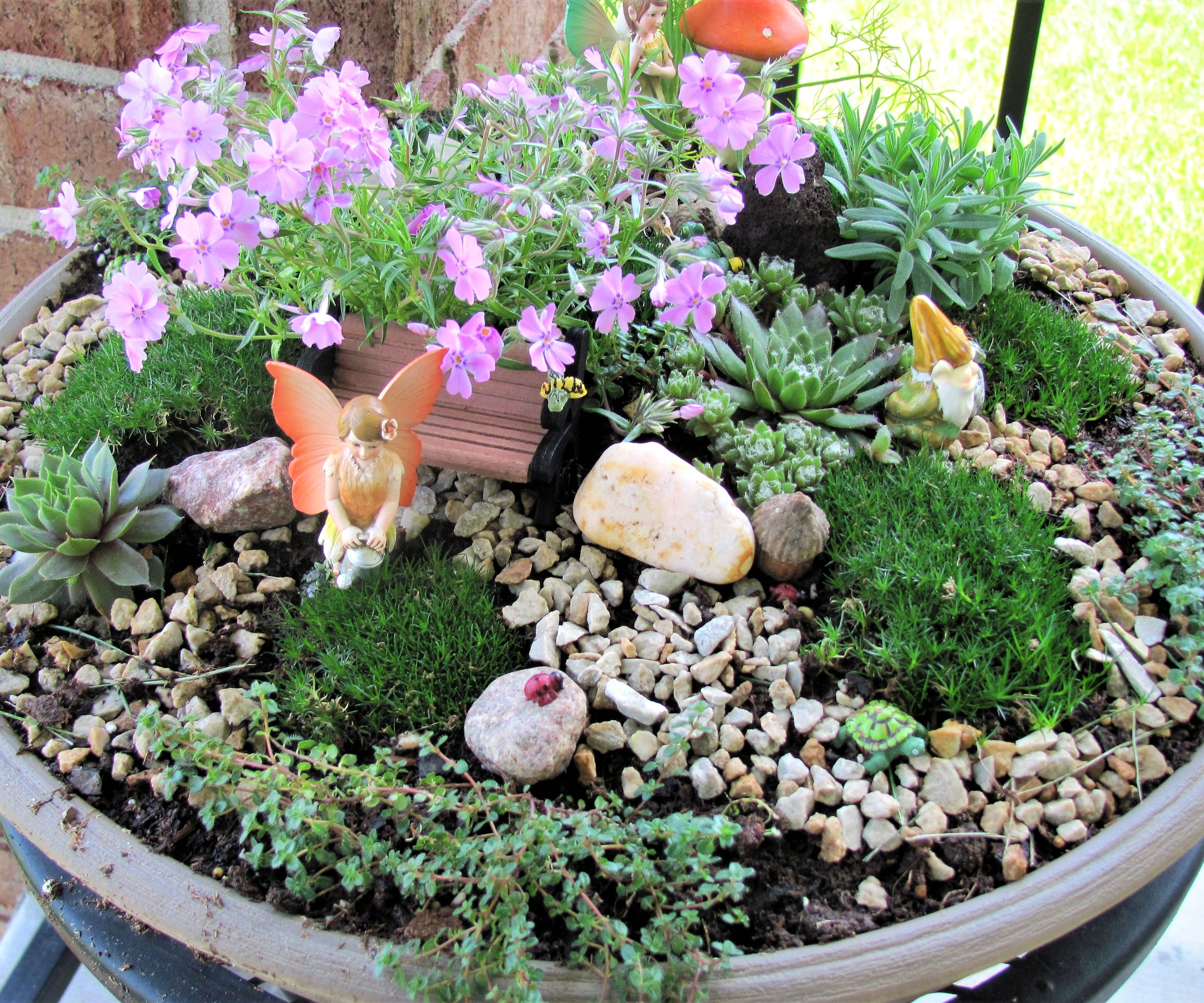 fairy garden container with pink plants, rocks and figurine