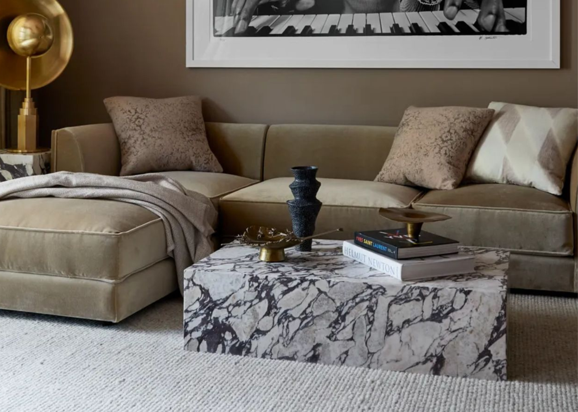 A marble coffee table styled with a black sculptural vase, books and decorative objects in front of a beige sofa with a throw and throw pillows and a large gold floor lamp