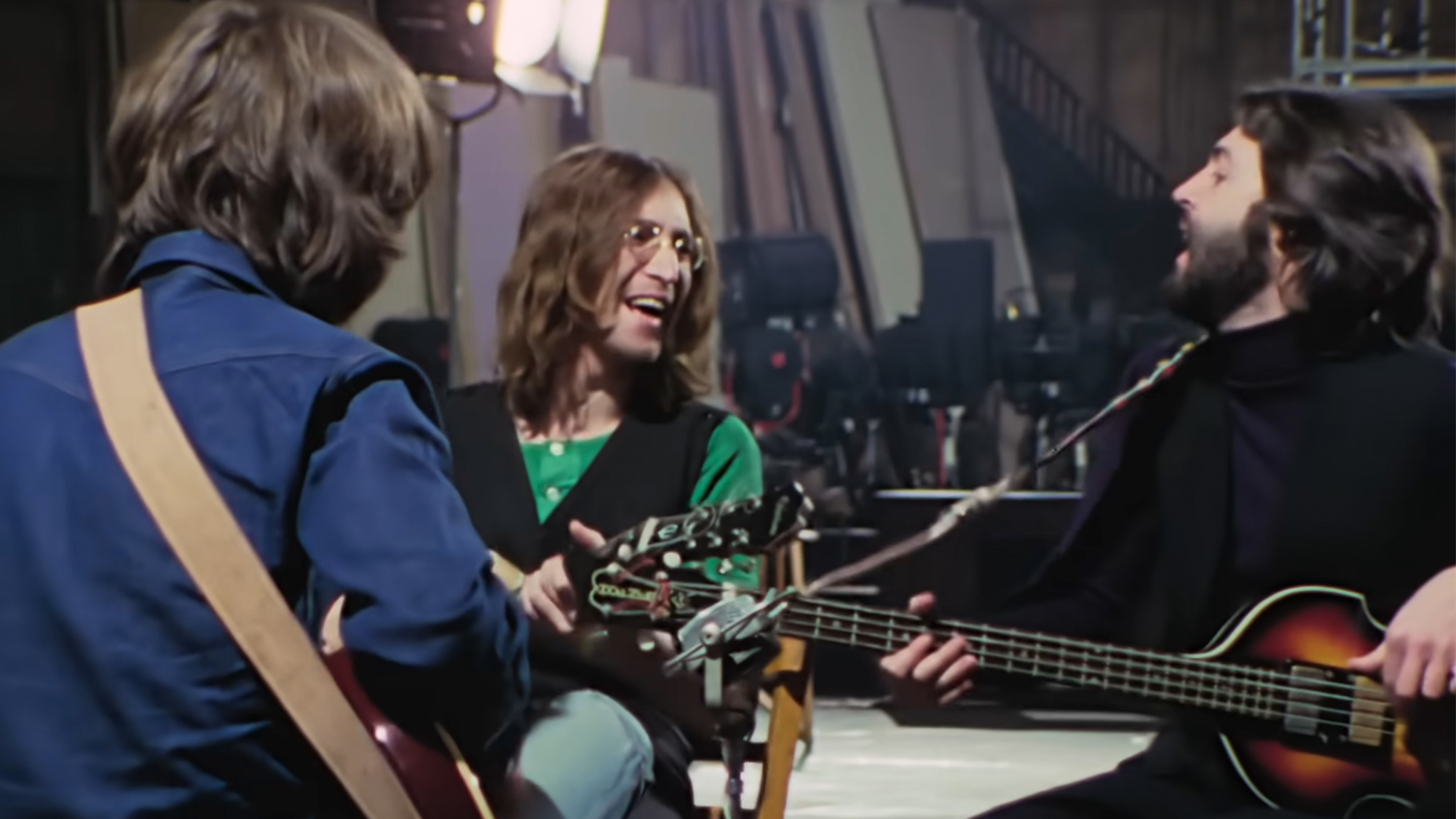 The Beatles singing and playing together, with George Harrison's back to the camera, in The Beatles: Get Back