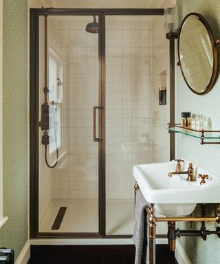 A shower room with a brass shower, mirror, white sink, and green walls
