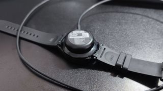 En svart Samsung Galaxy Watch 4 Classic som ligger på ett svart bord och laddas.