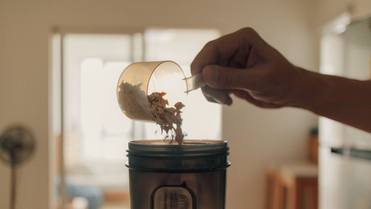 When is the best time to drink protein shakes? Image shows person loading protein powder into a shaker