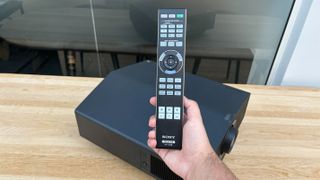 Sony Bravia Projector 9 on a light wood table with a hand holding a remote in the foreground