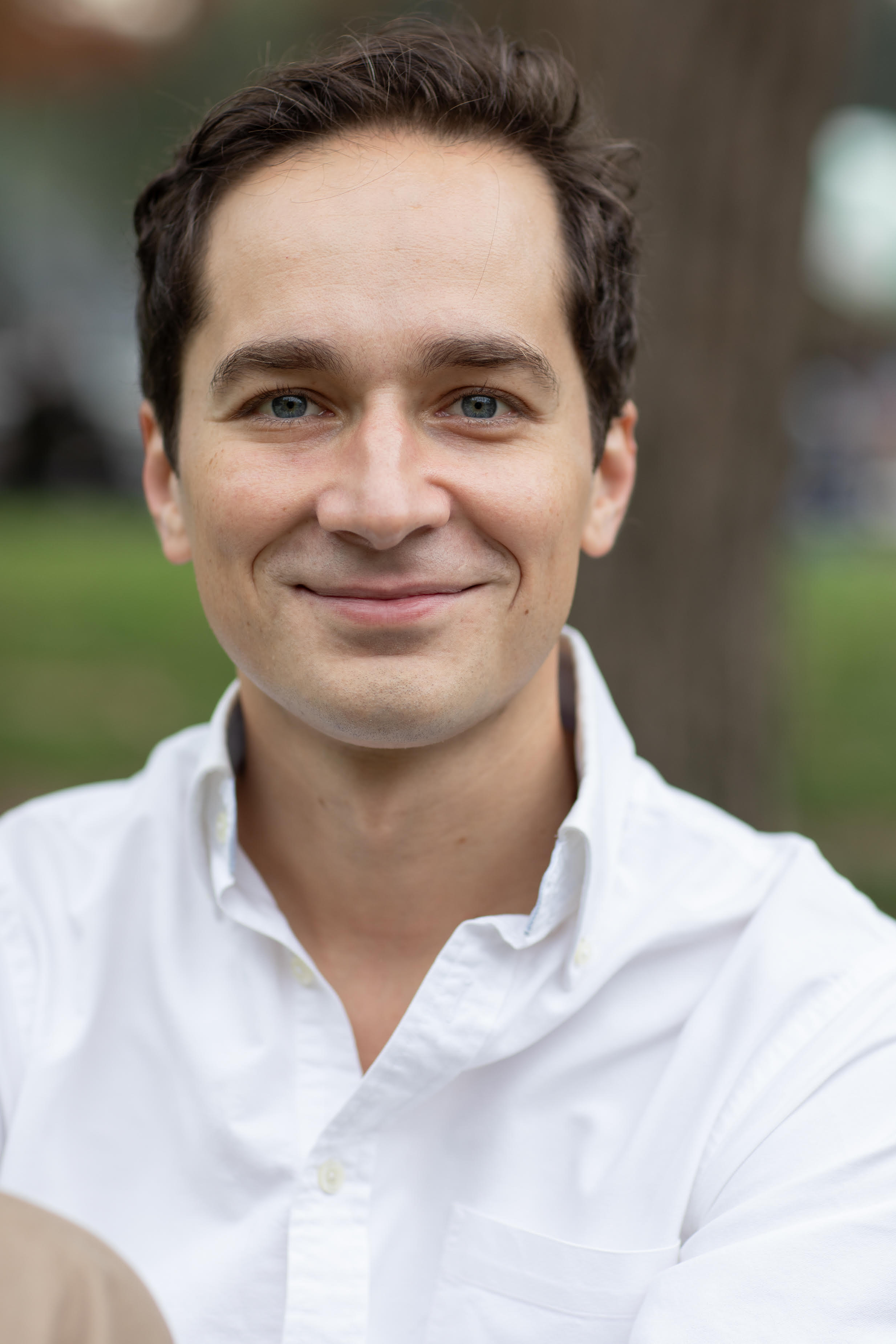 photo of a smiling man with short brown hair wearing a white button up