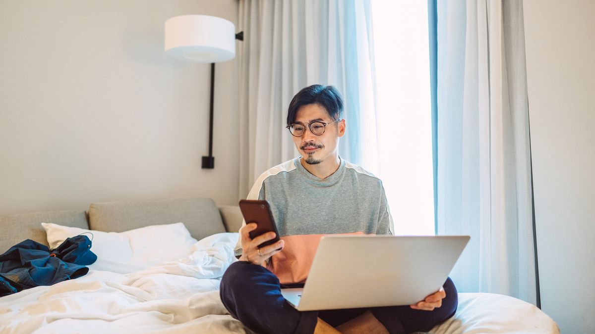 Young man using a smartphone and laptop in a hotel room