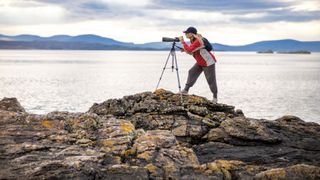 Woman looking through telescope on rocky ledge looking out to sea