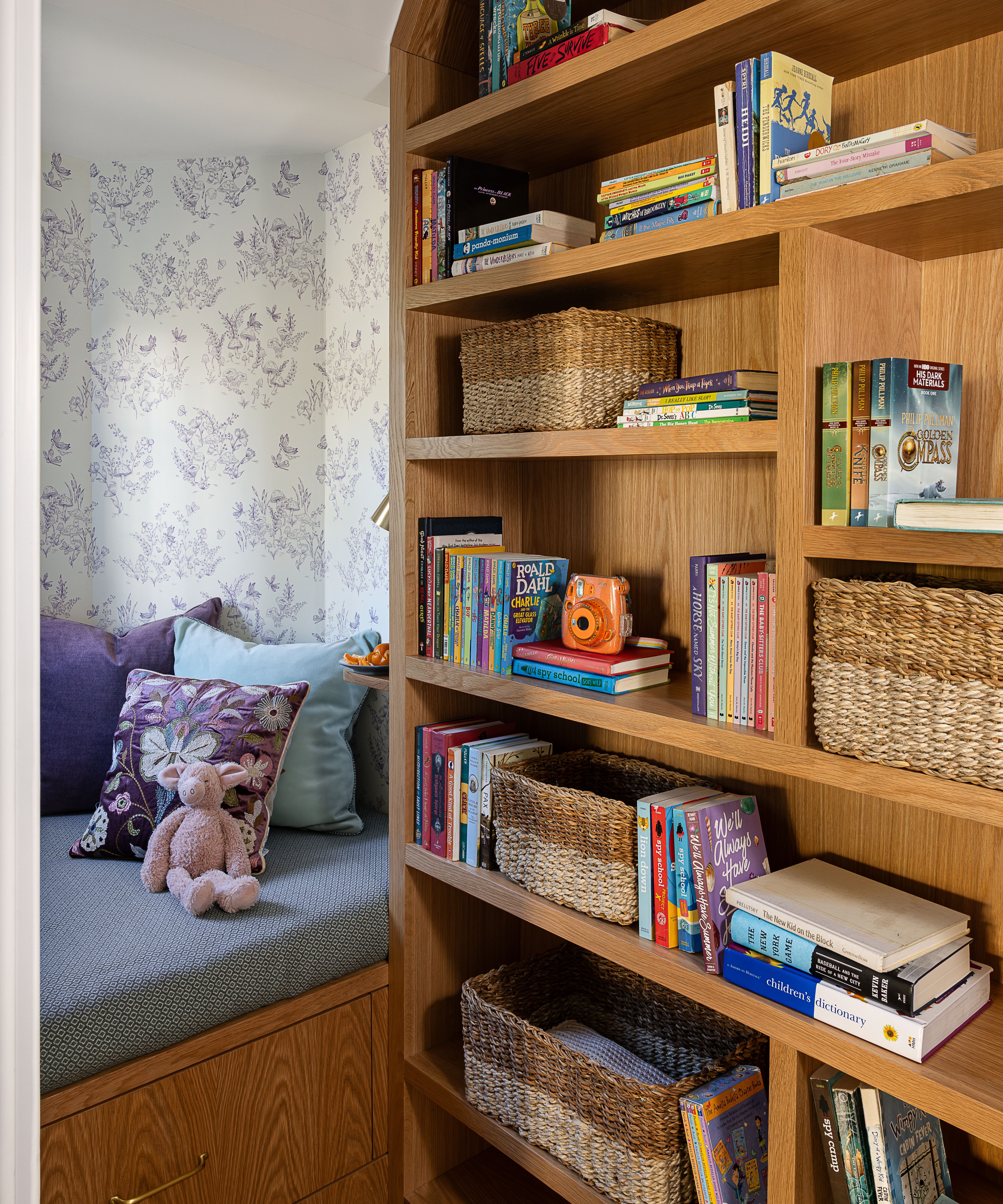 a kids room with a small built-in reading nook with purple floral wallpaper, a banquette, and curved bookshelves
