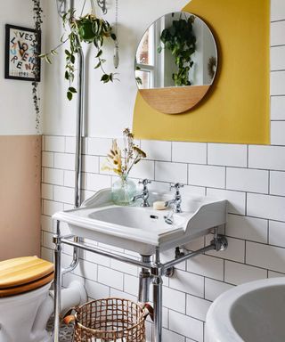 A modern traditional white bathroom with metro tile decor, yellow wall decor, white ceramic basin and set of two faucet taps with round mirror decor