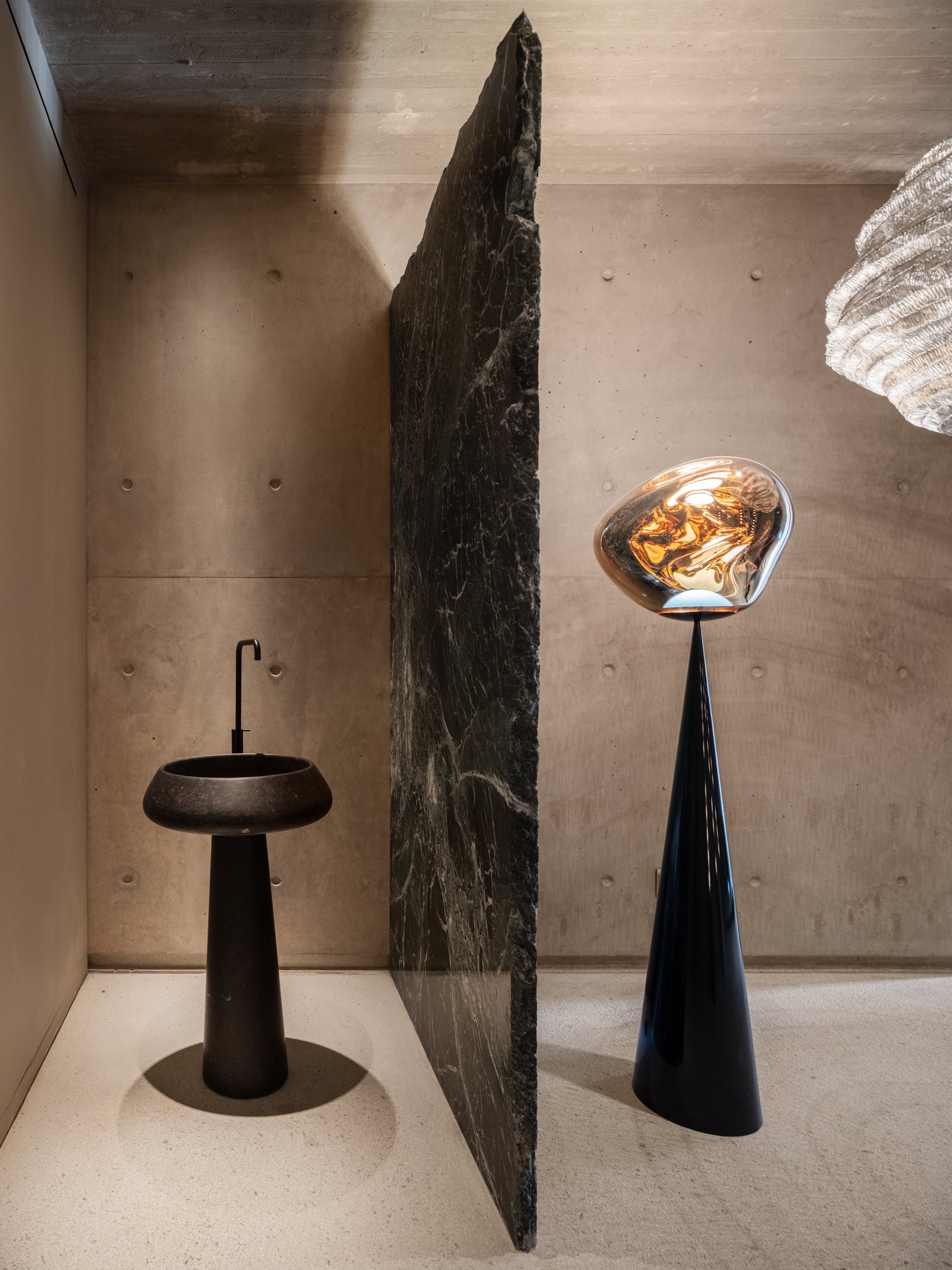 modern bathroom in brutalist home with concrete walls, pedestal sink, stone slab wall, tom dixon floor lamp