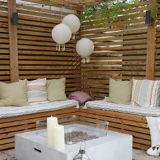 A pergola with built-in seating around a fire pit and three hanging outdoor lantern lights