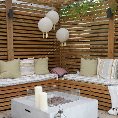 A pergola with built-in seating around a fire pit and three hanging outdoor lantern lights