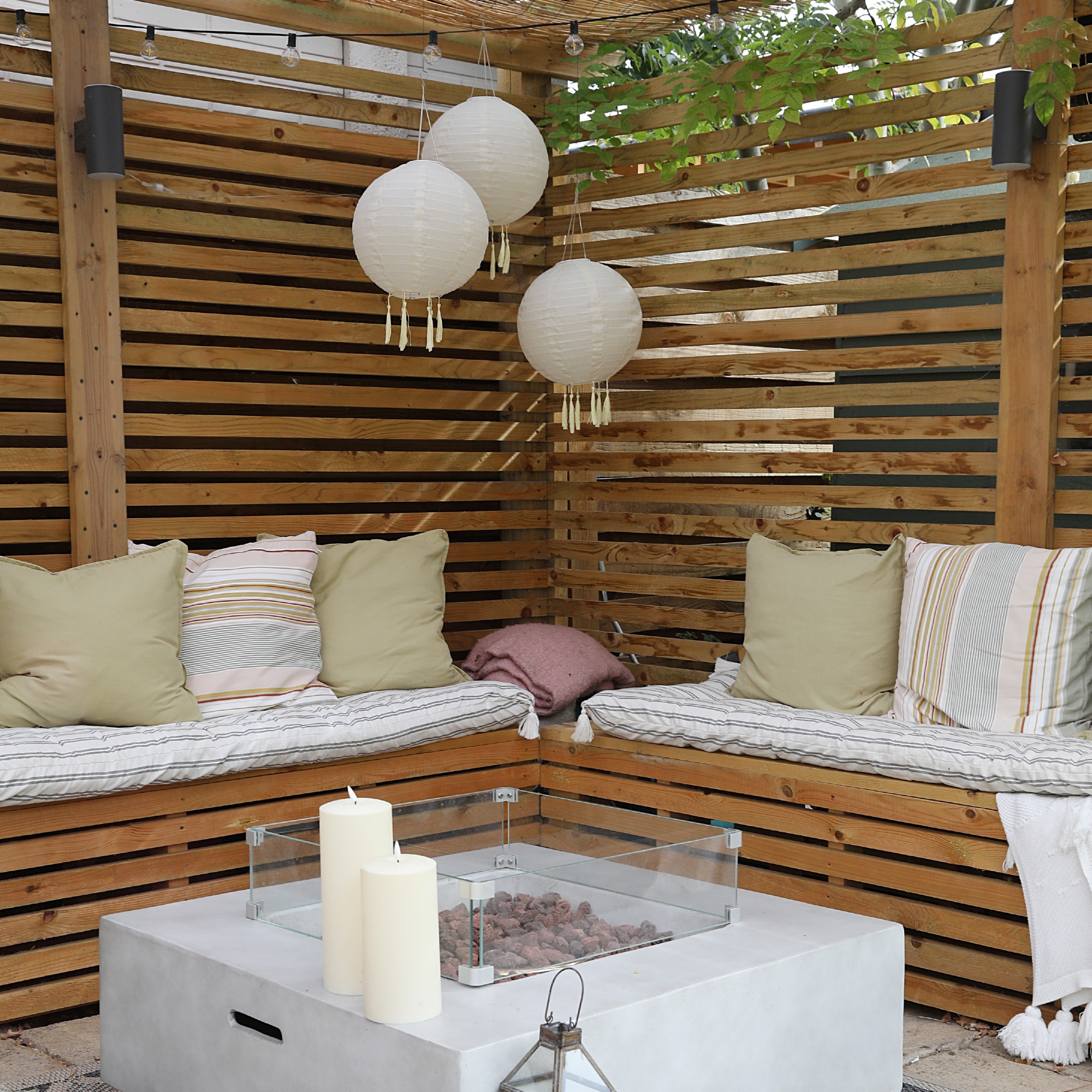 A pergola with built-in seating around a fire pit and three hanging outdoor lantern lights