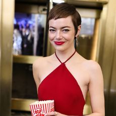Emma Stone wearing red lipstick and a red dress, smiling at a camera