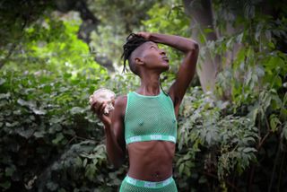 A black woman in a mint green see-through mesh workout set is posing with a sea shell in her right hand.