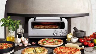 Breville The Smart Oven Pizzaiolo surrounded by different pizzas, garlic, tomatoes, bread and oil