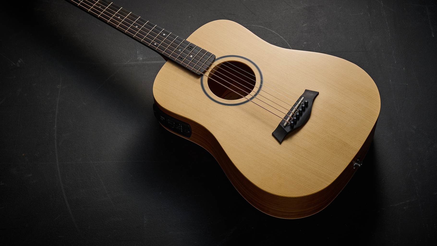 A Taylor BT1e Baby Taylor 3/4 acoustic guitar lying on a black floor