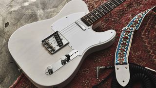 White Fender Telecaster on a carpet next to a colourful guitar strap