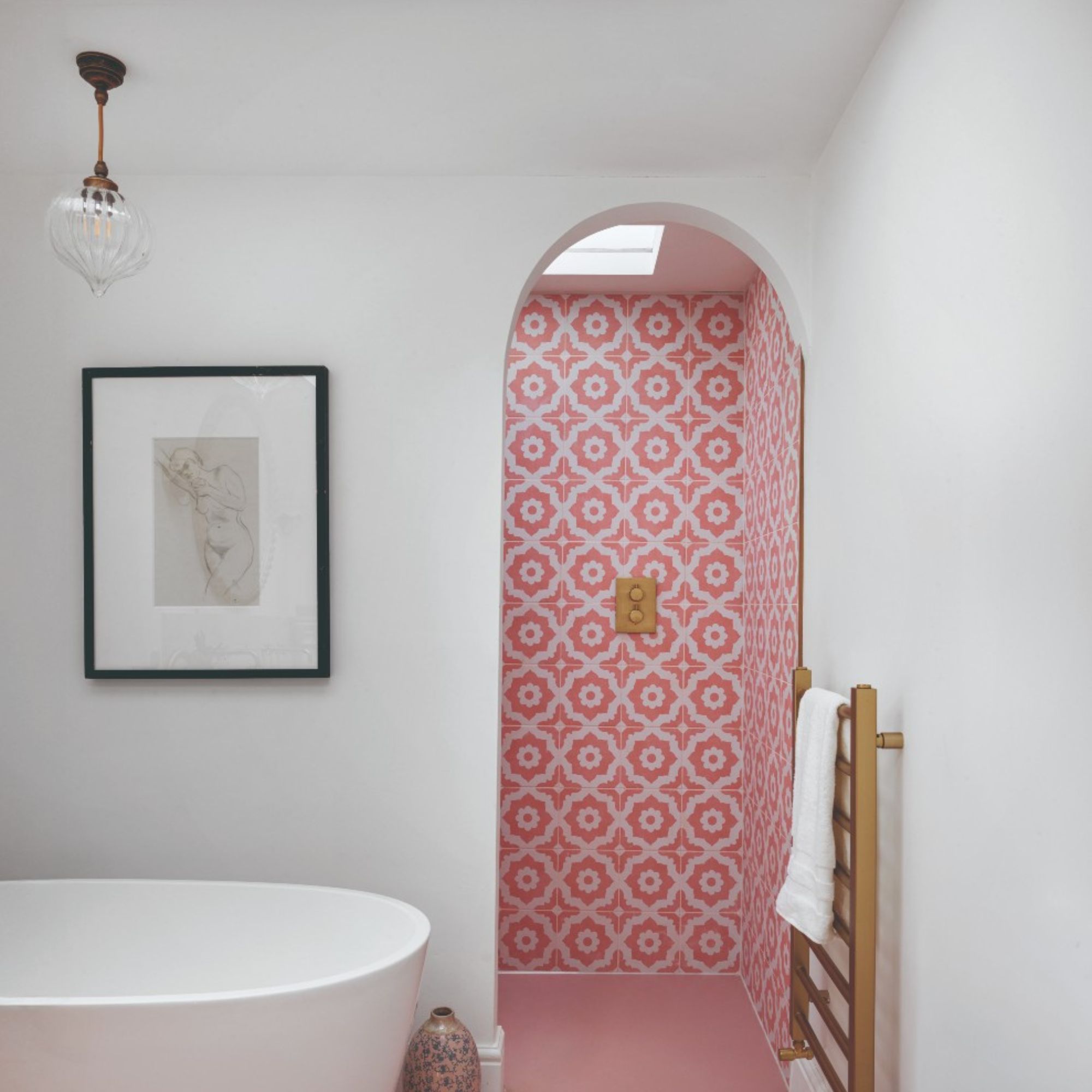 White en suite with freestanding bath tub, arched walkway into pink tiled shower with gold accents