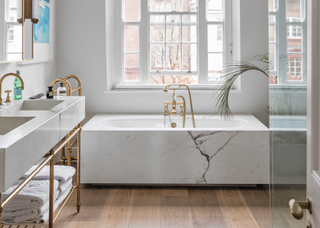 A bathroom with a marble bathtub and wooden floor