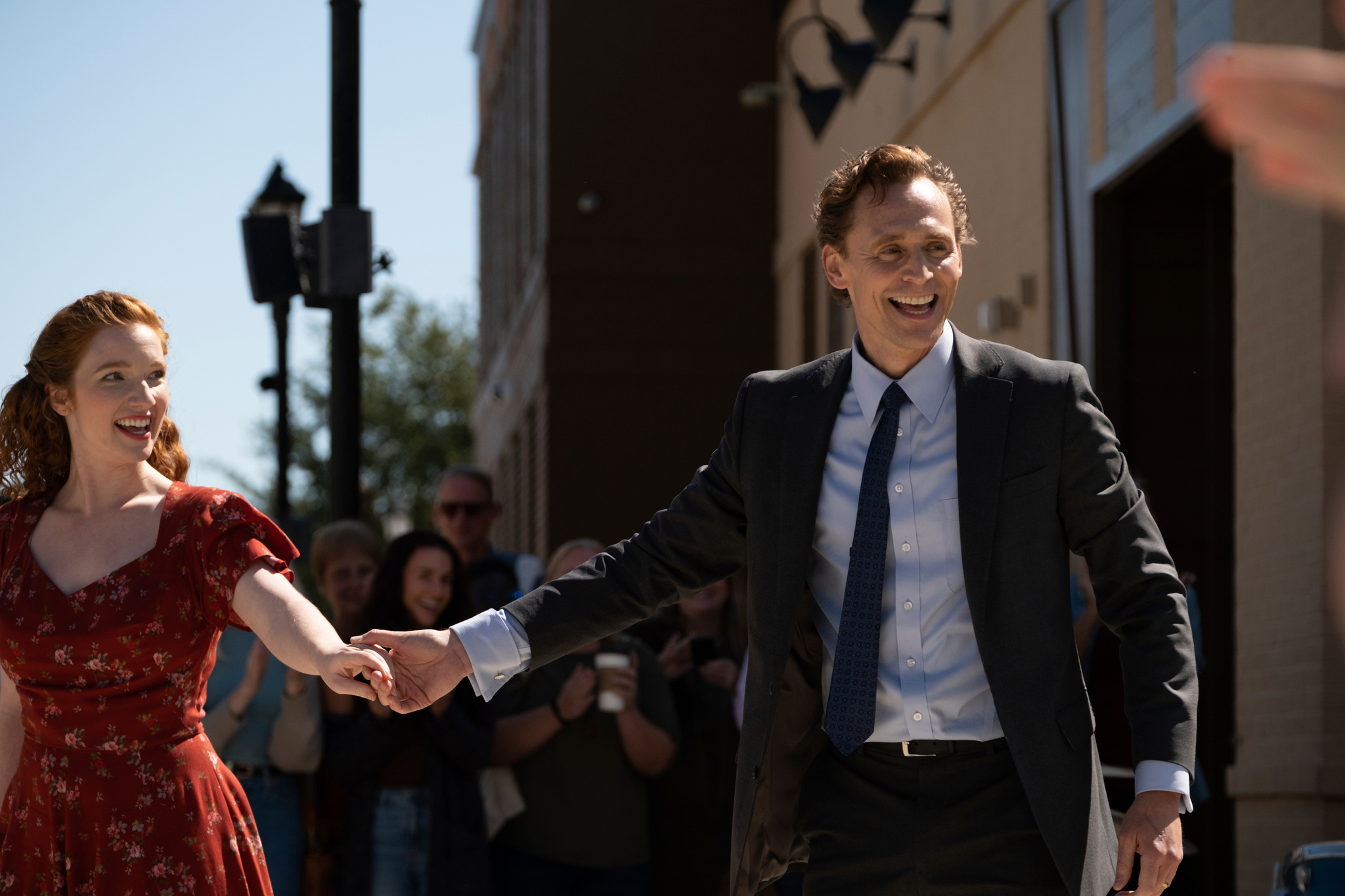 Annalise Basso and Tom Hiddleston, holding hands and smiling while standing in front of a crowd, in 'The Life of Chuck.'