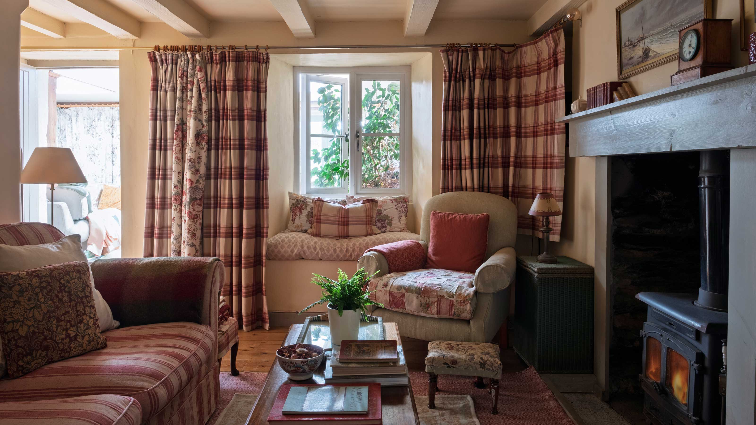 cosy living room in a country cottage with check curtains, wood burner, window seat and comfy armchairs