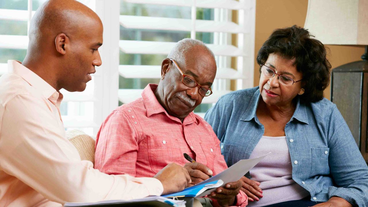 Photograph of a man talking to an older couple over some paperwork.