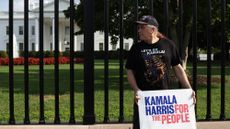 A man holds a Kamala Harris campaign sign outside the White House fence 