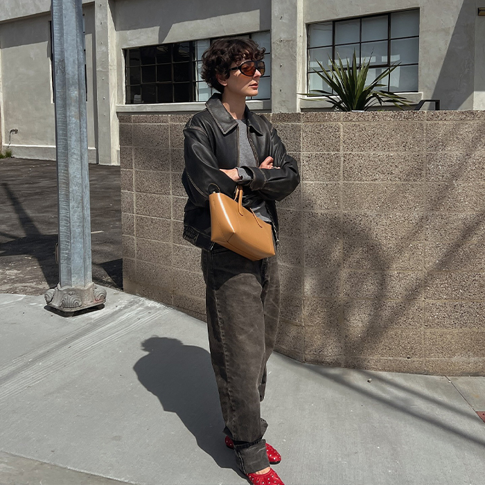 Alyssa wears bomber, gray shirt, and slouchy jeans, red flats, and a tan purse