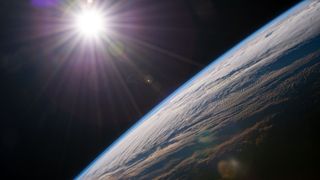 view of the bright sun over the curve of the edge-on earth, with the thinness of the atmosphere apparent
