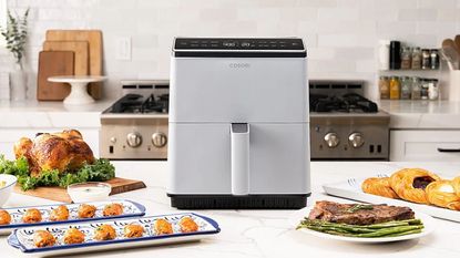 Ninja vs Cosori: one of the best Cosori air fryers, the Cosori Dual Blaze IIon a countertop with chicken and pastries around it