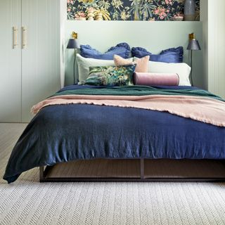 a green bedroom with fitted wardribes and a section of bold floral wallpaper above a bed covered in navy and pink bedlinen