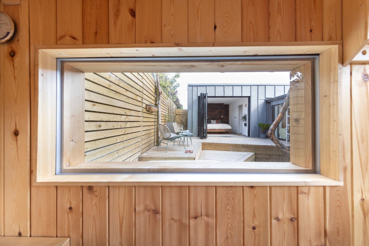The view from inside a home sauna looking out over a decking area with a hot tub