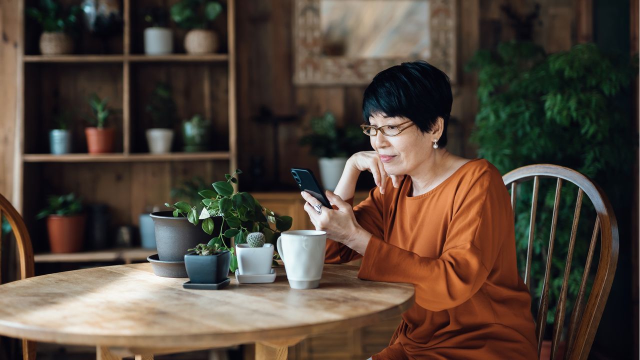 An older woman looks at her smartphone at her kitchen table.