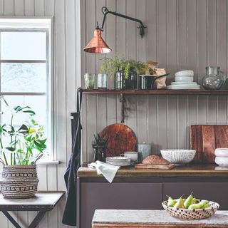 A kitchen with grey-painted wall panels and open shelving on top of it