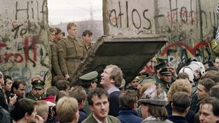 East German soldiers preparing to pass through a hole in the Berlin wall as crowds celebrate