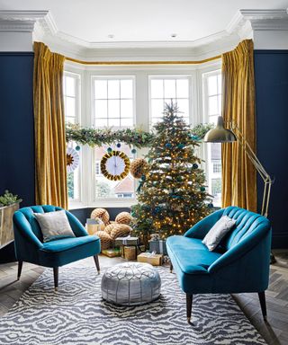 Christmas tree themes 2021 with gold and blue baubles in a bloue and gold modern living room