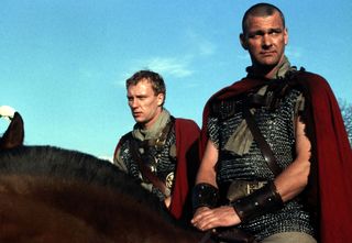 two men in ancient roman clothes riding horses in a still from rome