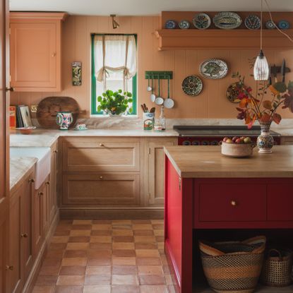 kitchen with terracotta painted walls, wooden floor cabinets and red painted island, with terracotta chequerboard tiles