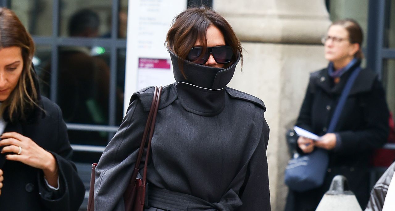 Victoria Beckham walks around Paris wearing a high neck trench coat with a tote bag over her shoulder