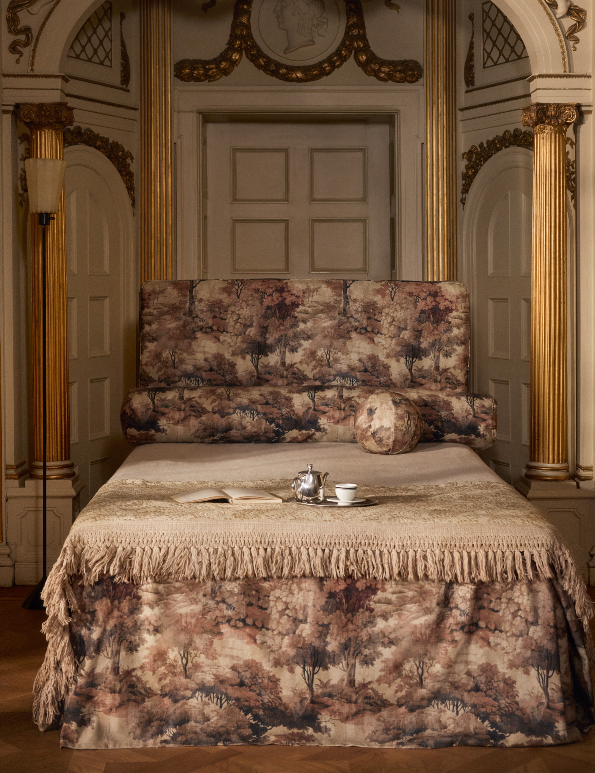 Opulent bedroom with green-and-gold gilded walls featuring a tapestry print covered bed, which is styled with a book and tea set
