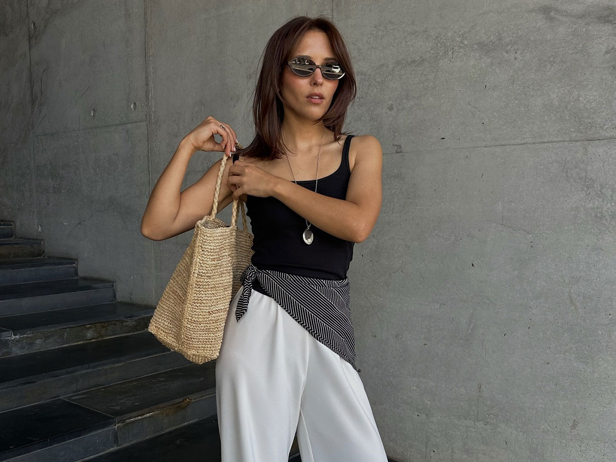 @deborabrosa wearing a black tank, white trousers, and a printed scarf around her waist.