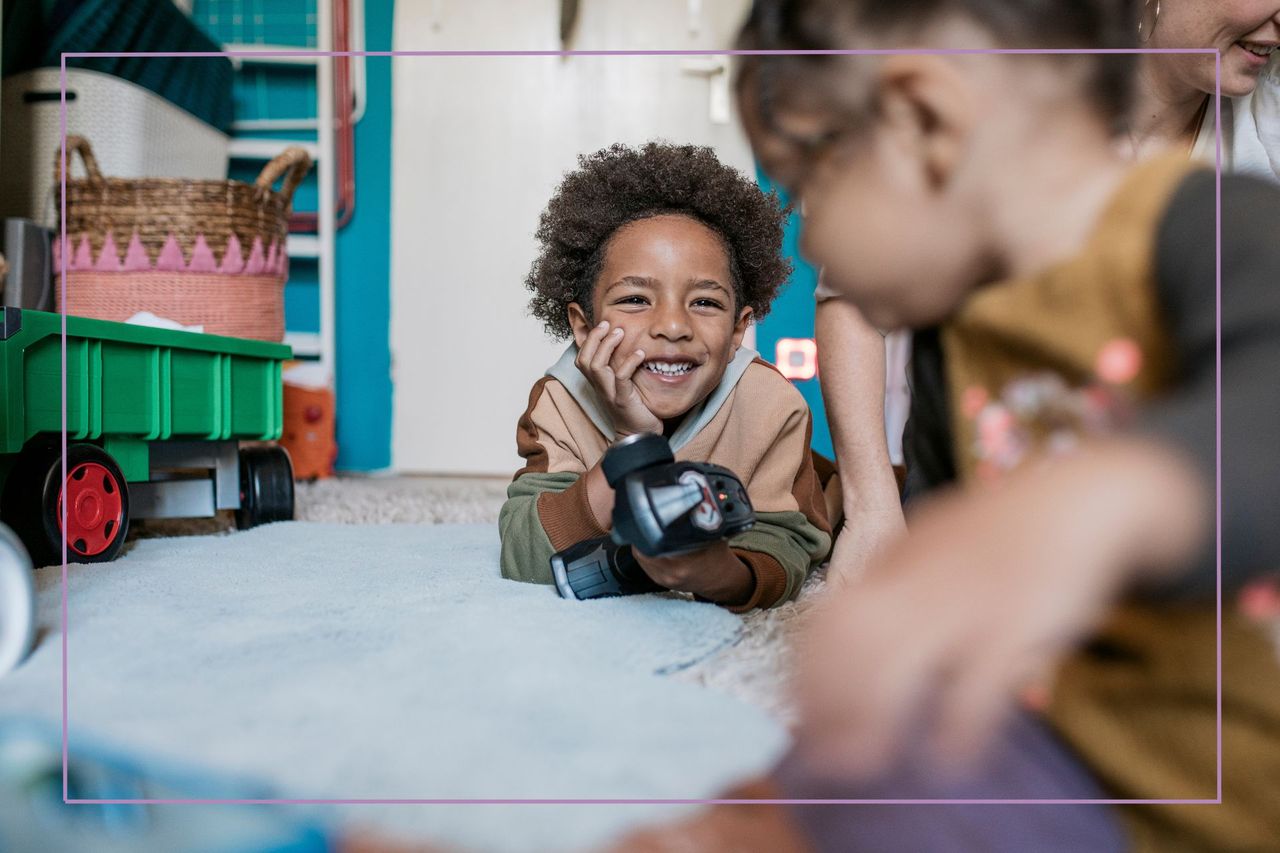 A young boy smiling while playing on the carpet in the bedroom with his family