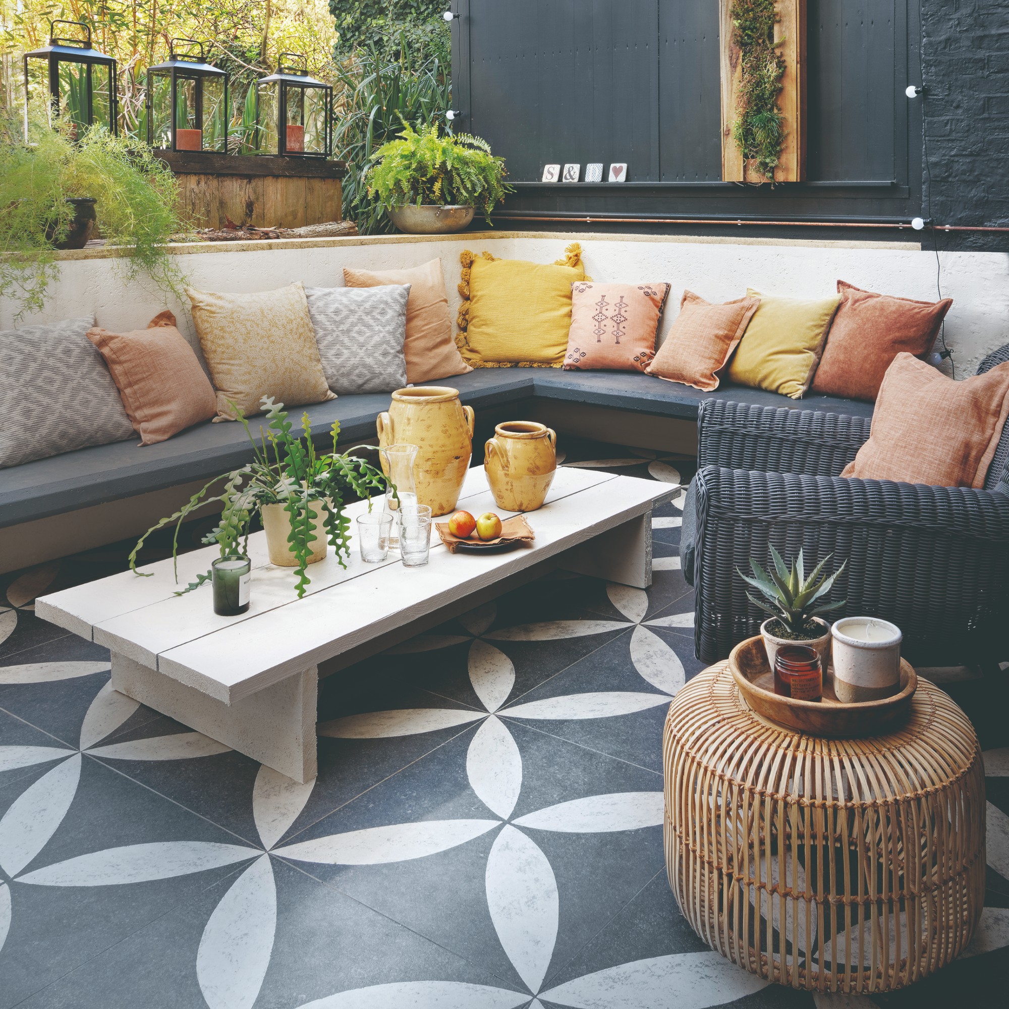 A patio with a built-in corner bench seating with grey seat cushions and scatter cushions in ochre yellows and terracotta shades
